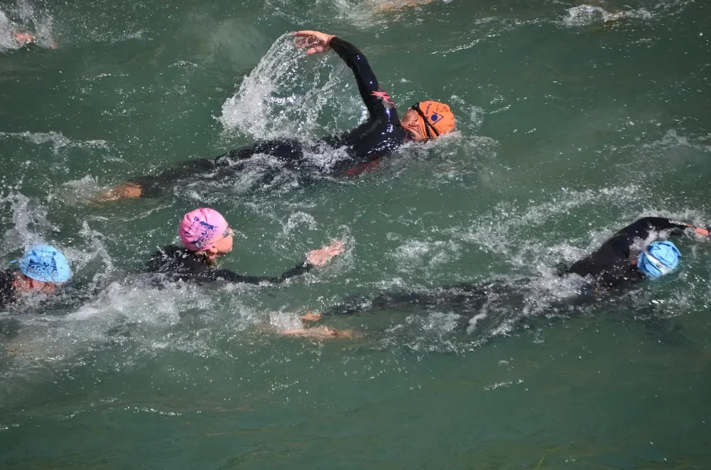 Pływacy w piankach i czepkach płyną kraulem w otwartej wodzie podczas triathlonu