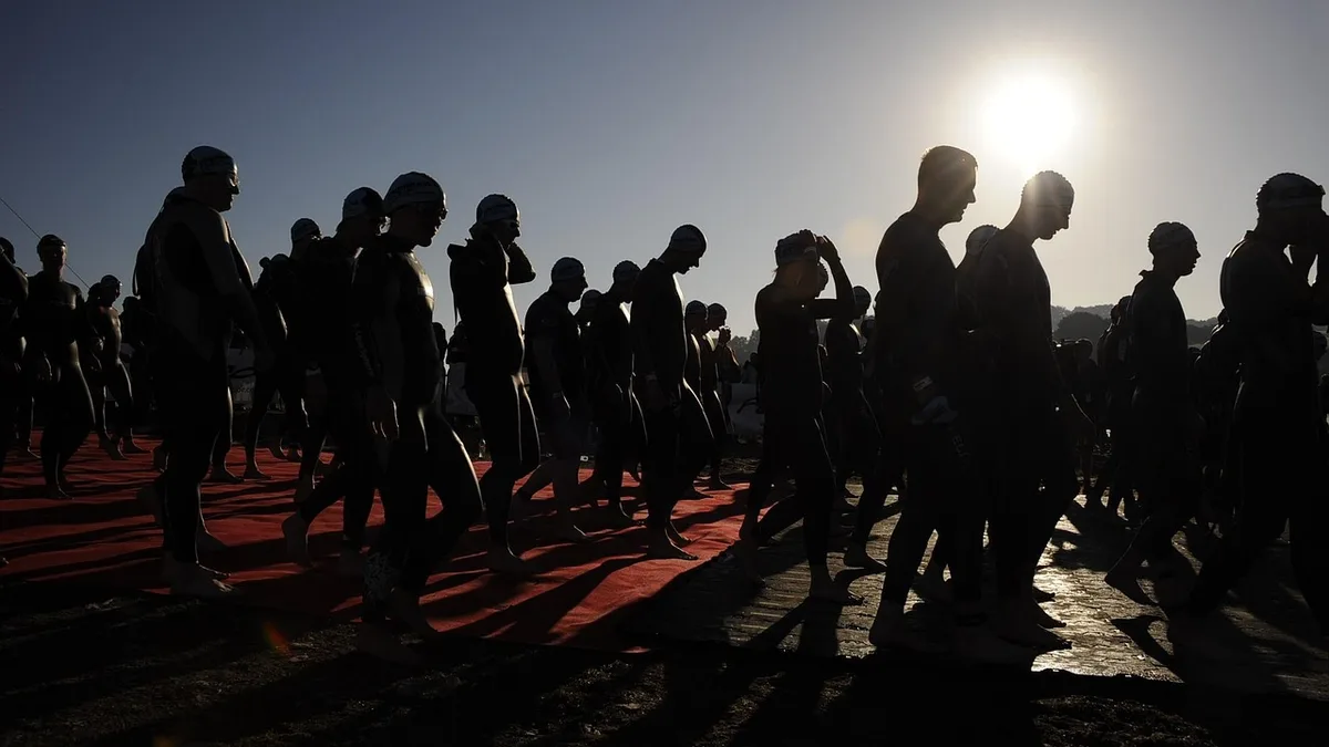 Zawodnicy w piankach idą na start triathlonu o wschodzie słońca przed dystansem 1/8 Ironman