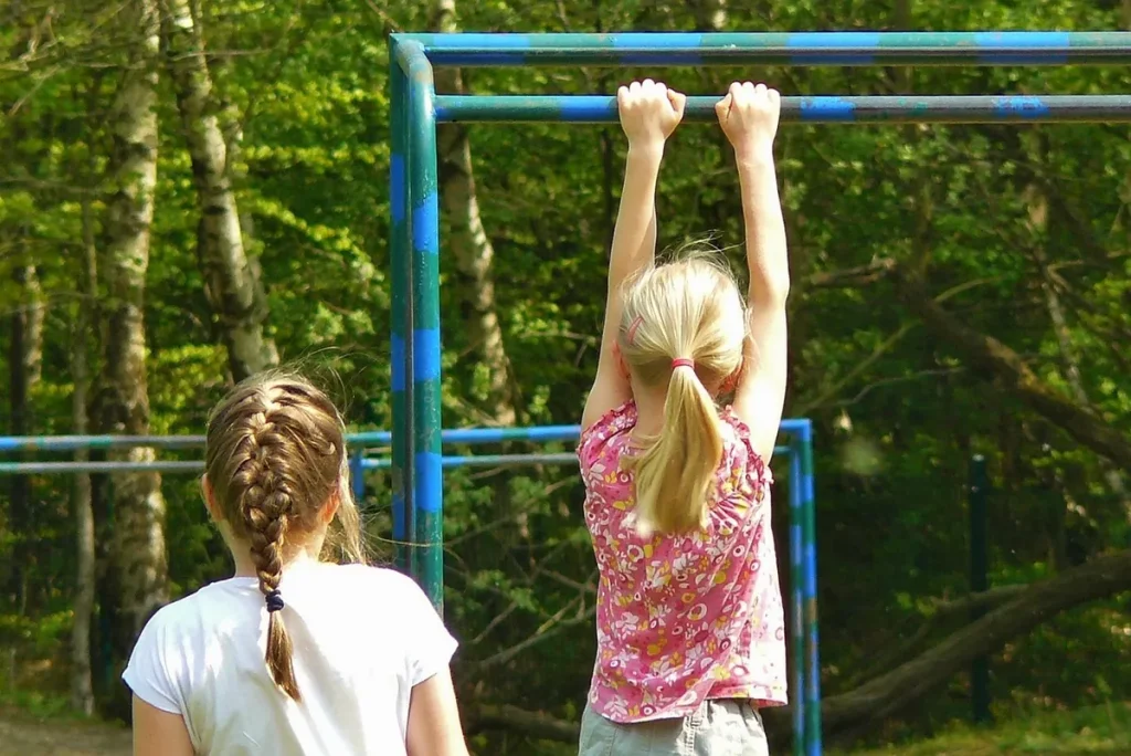 Dziewczynka w zwisie na drążku na placu zabaw — siła jako jedna ze zdolności kondycyjnych